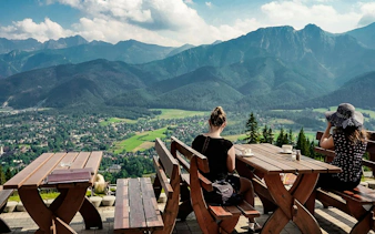Benches overlooking Tatra Mountains in Zakopane, Poland, with visitors enjoying the view.