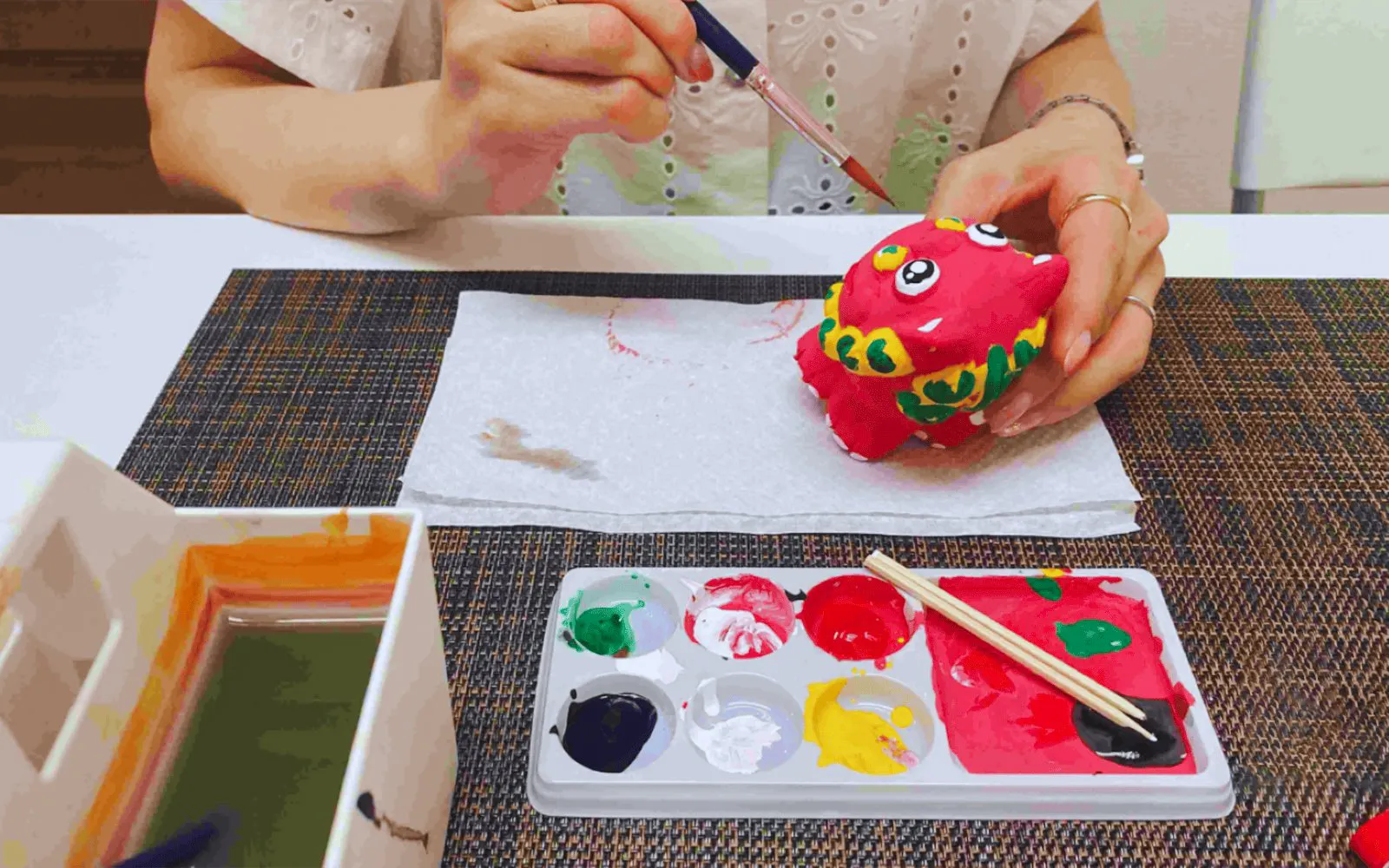 Woman painting a red Shisa figurine with colorful paints in Okinawa.