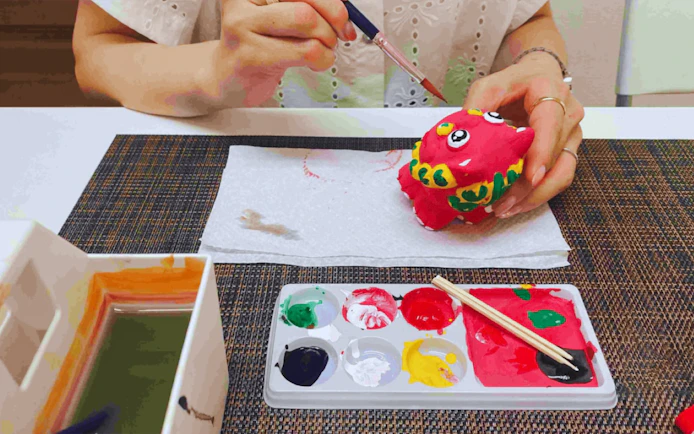 Woman painting a red Shisa figurine with colorful paints in Okinawa.