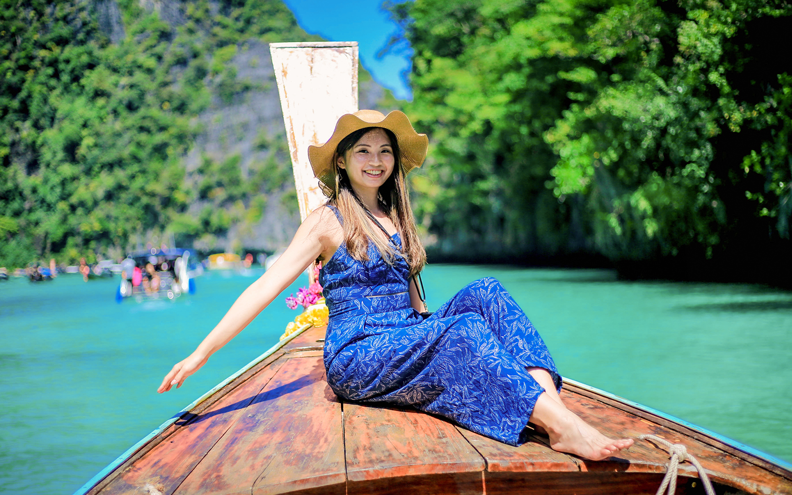 Woman on a boat enjoying Phi Phi Islands tour, turquoise water and lush greenery in background.
