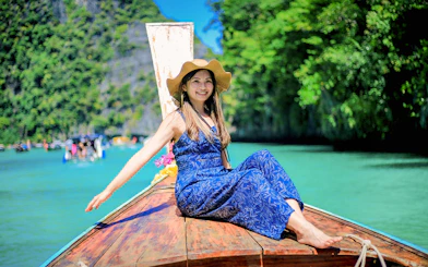Woman on a boat enjoying Phi Phi Islands tour, turquoise water and lush greenery in background.