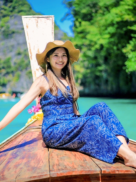 Woman on a boat enjoying Phi Phi Islands tour, turquoise water and lush greenery in background.