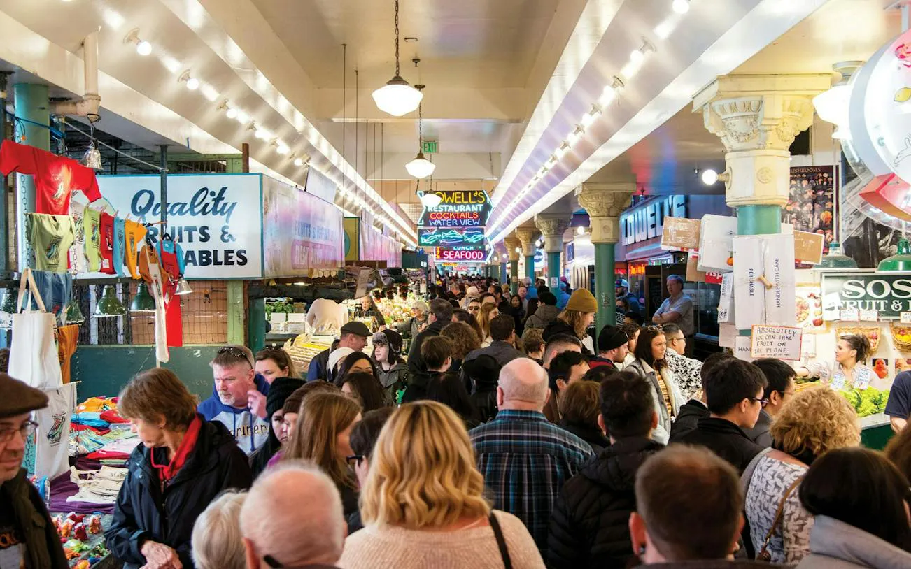 Crowded Pike Place Market in Seattle with people exploring stalls and neon signs.
