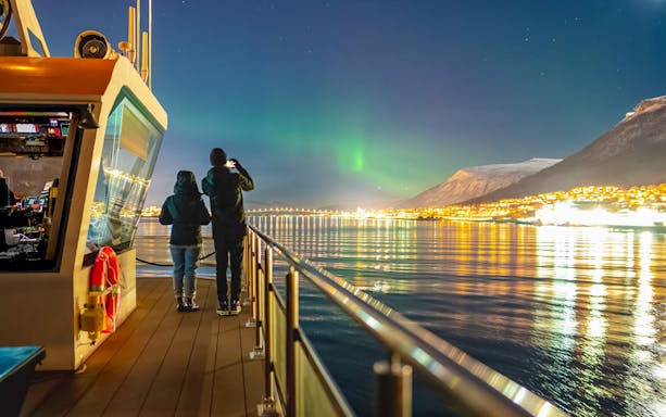 Couple on deck viewing Northern Lights during Aurora Boreal dinner cruise.