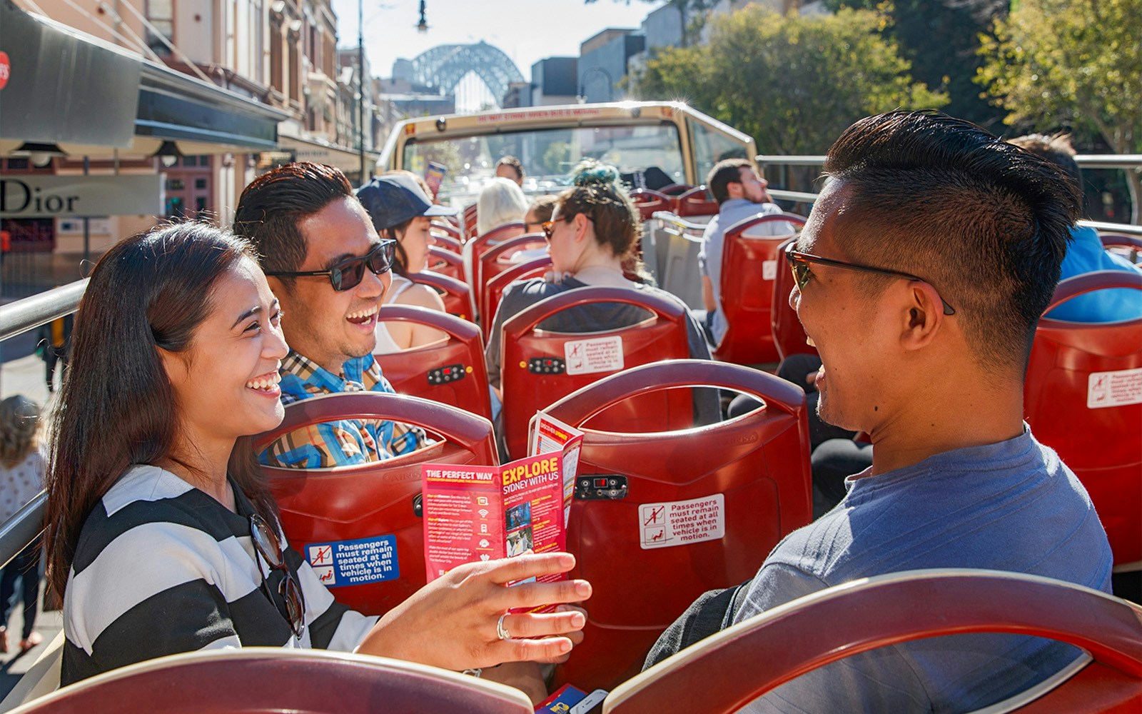 Passengers enjoying a ride on Big Bus Sydney with Sydney Harbour Bridge in the background.