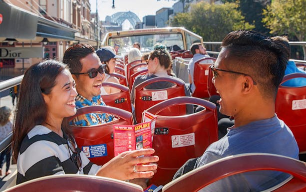 Passengers enjoying a ride on Big Bus Sydney with Sydney Harbour Bridge in the background.