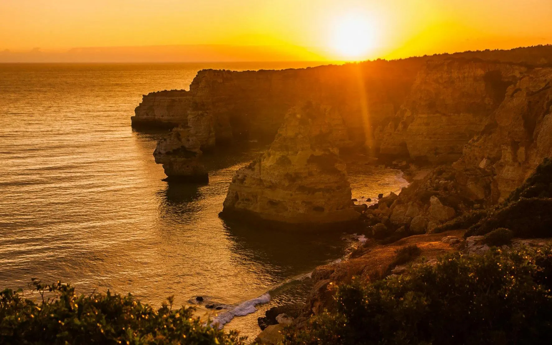 Algarve coastline at sunset with cliffs and ocean view.