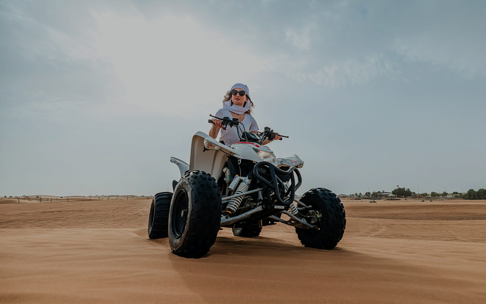 Person riding a quad bike on desert sand during an evening safari adventure.