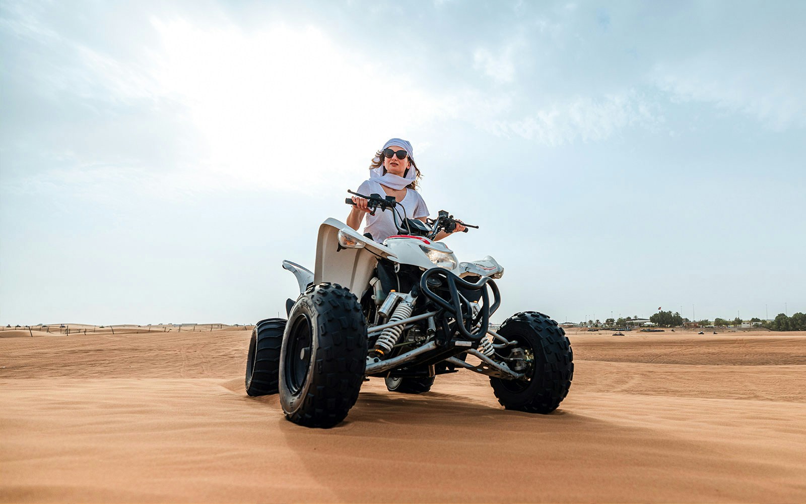 Person riding a quad bike on desert sand during an evening safari adventure.