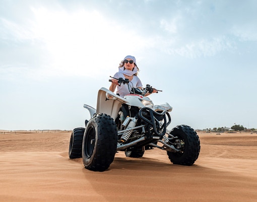 Person riding a quad bike on desert sand during an evening safari adventure.