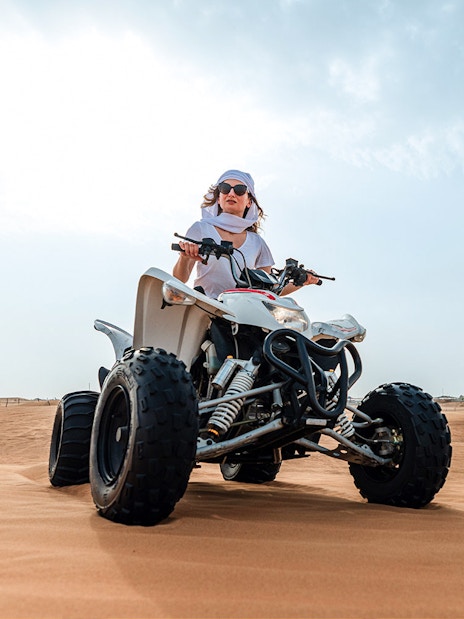 Person riding a quad bike on desert sand during an evening safari adventure.