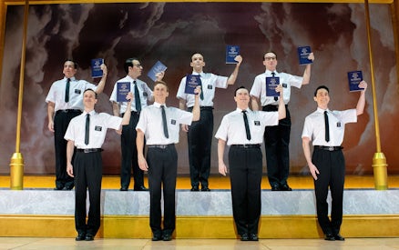 Performers holding books on stage in "The Book of Mormon" musical.