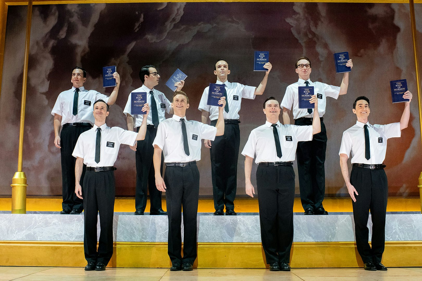 Performers holding books on stage in "The Book of Mormon" musical.
