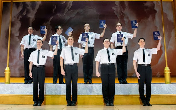 Performers holding books on stage in "The Book of Mormon" musical.