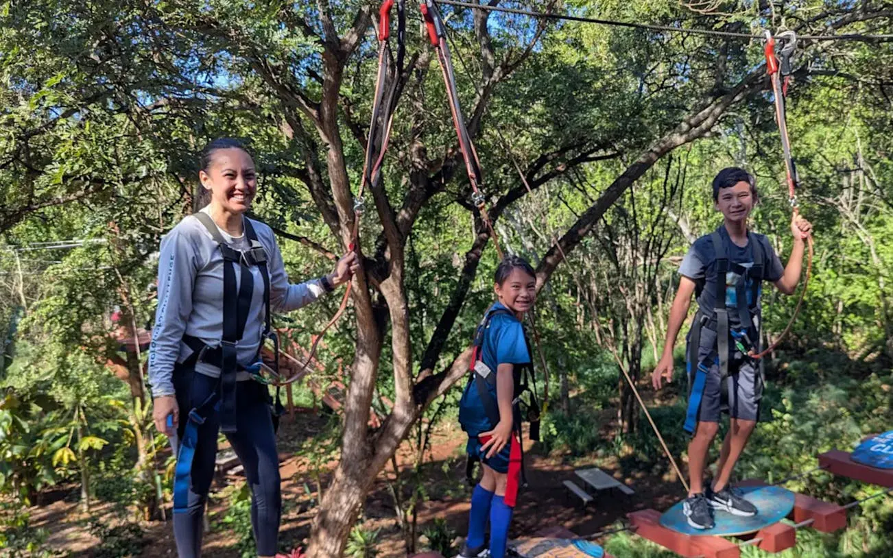 Participants navigating high-elevation adventure course with safety gear in a forest setting.
