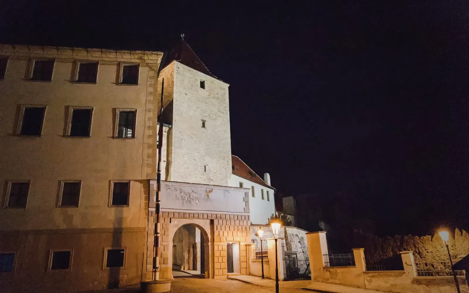 Prague Castle at night with illuminated stone tower and archway entrance.