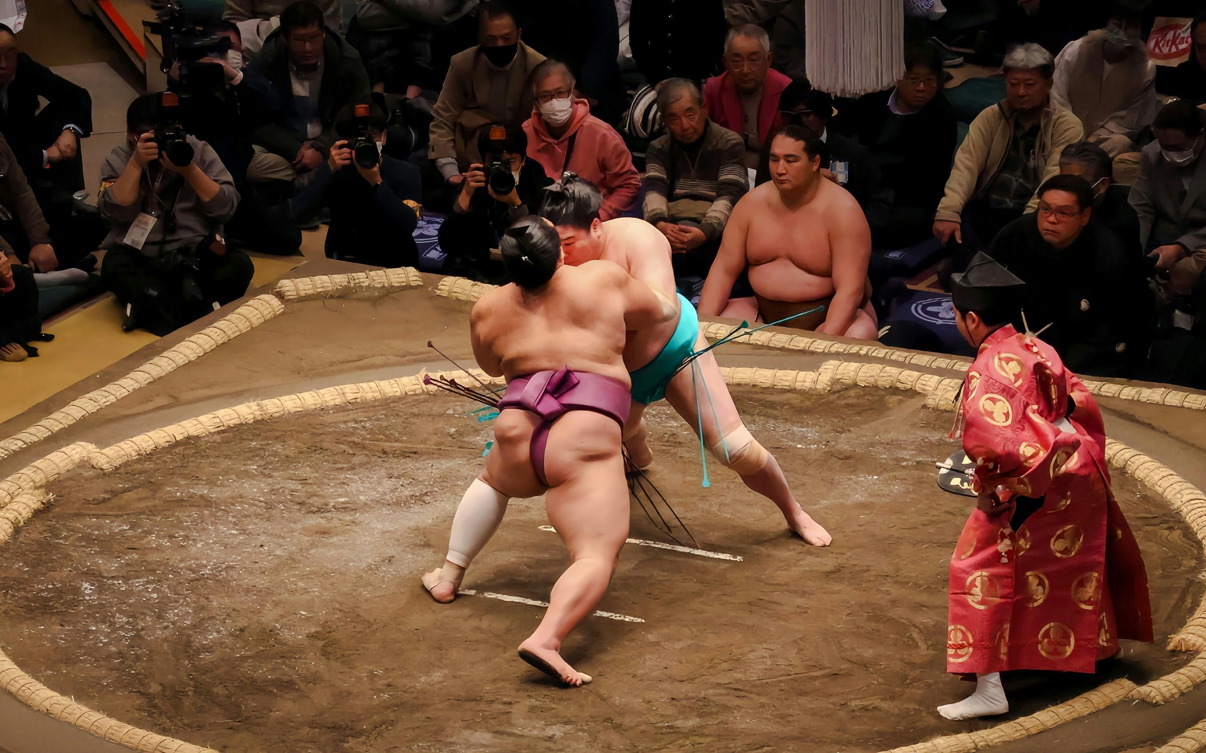 Sumo wrestlers grappling in a traditional ring during a match in Japan.