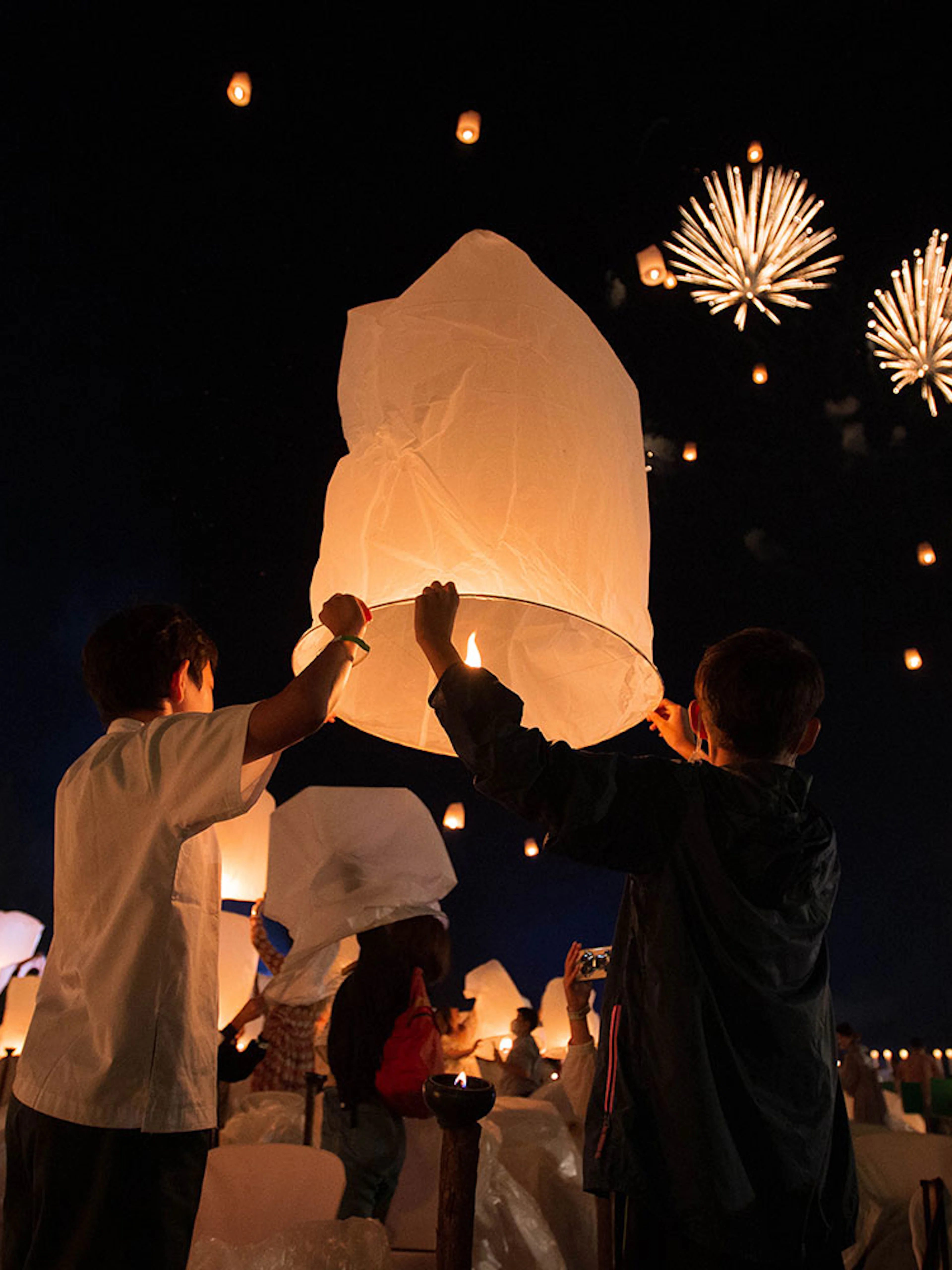 Participants release lanterns at Yeepeng Lanna Festival 2023 with fireworks in the night sky.