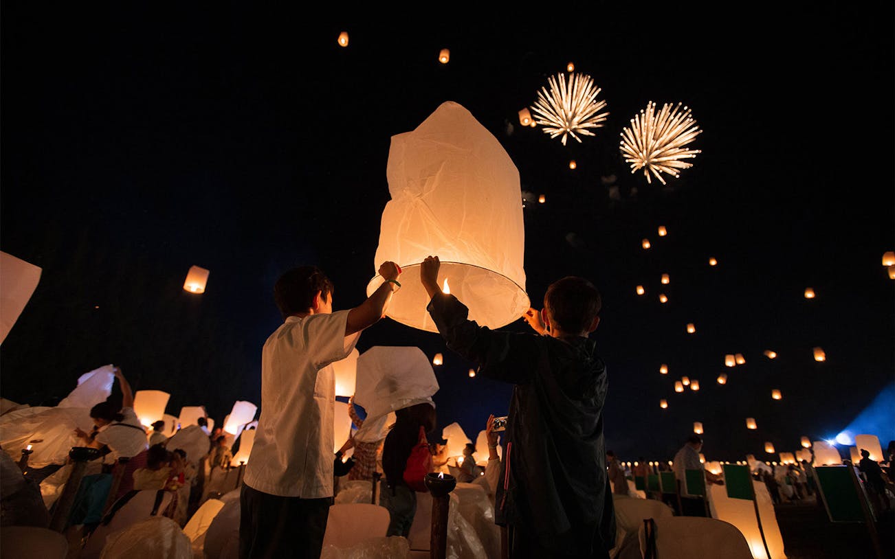 Participants release lanterns at Yeepeng Lanna Festival 2023 with fireworks in the night sky.