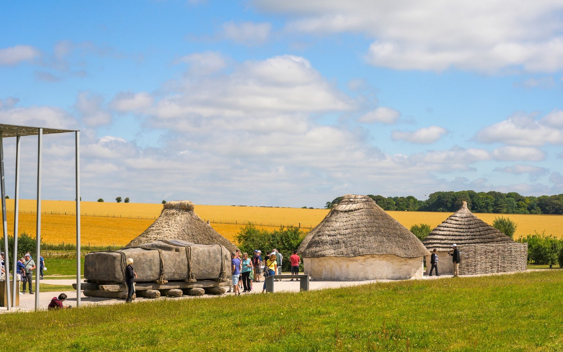 Neolithic huts near Stonehenge, England, with visitors exploring the site.