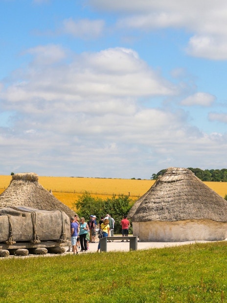 Neolithic huts near Stonehenge, England, with visitors exploring the site.