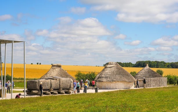 Neolithic huts near Stonehenge, England, with visitors exploring the site.