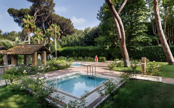Pool and gardens at QC Terme Roma Resort & Spa, Italy, surrounded by lush greenery.