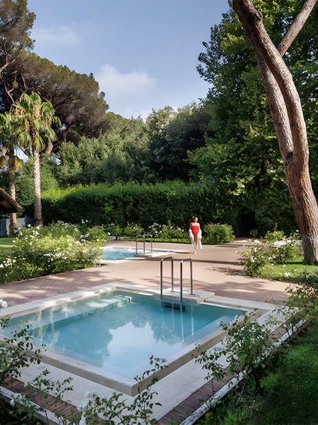 Pool and gardens at QC Terme Roma Resort & Spa, Italy, surrounded by lush greenery.