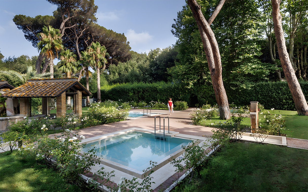 Pool and gardens at QC Terme Roma Resort & Spa, Italy, surrounded by lush greenery.