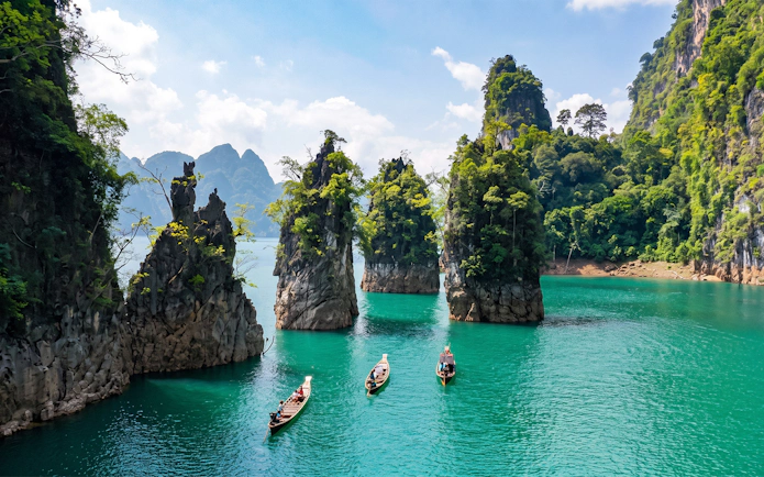 Boats on Cheow Lan Lake surrounded by limestone cliffs and lush jungle in Krabi, Thailand.
