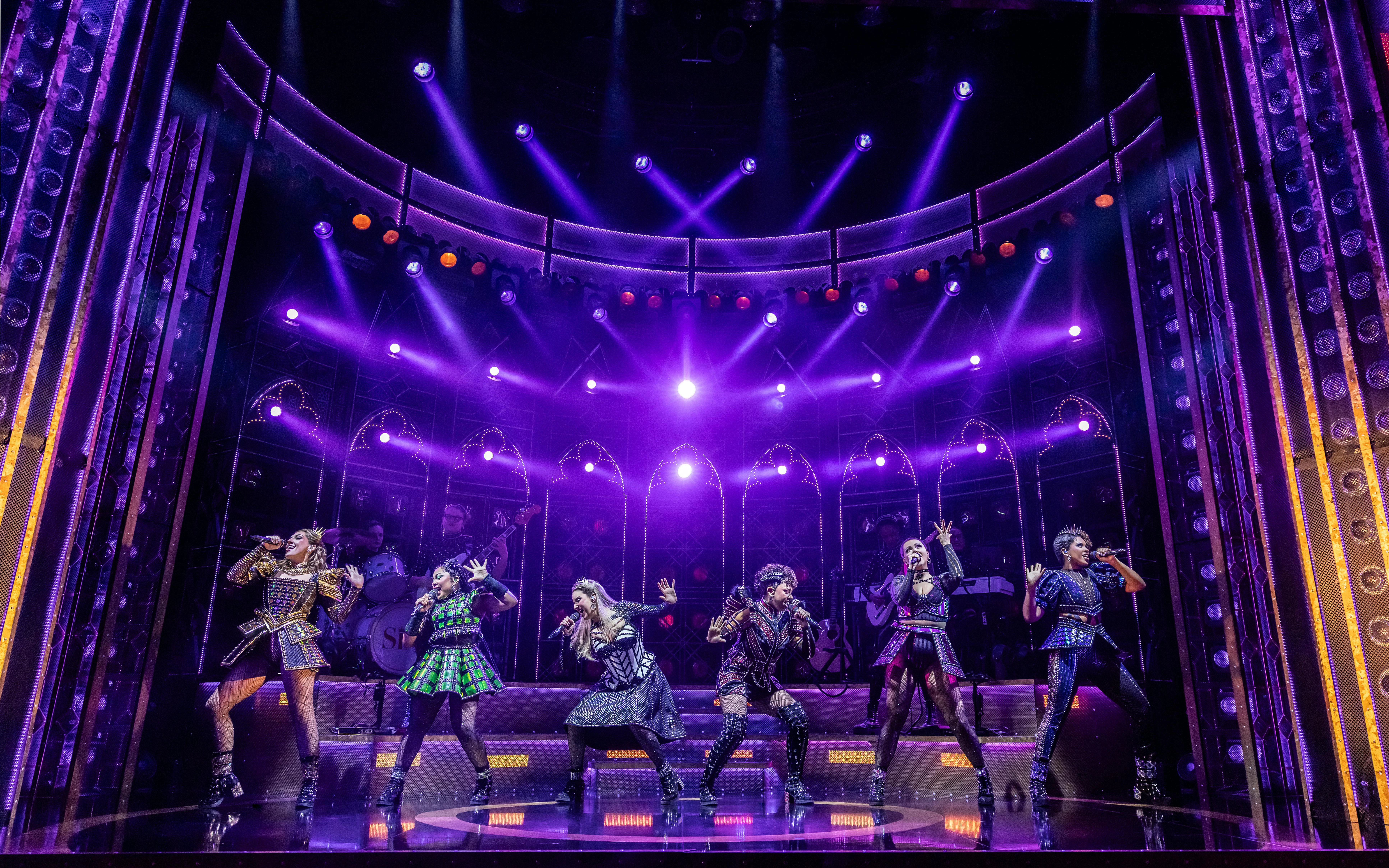 Six musical performance on West End stage with vibrant lighting.