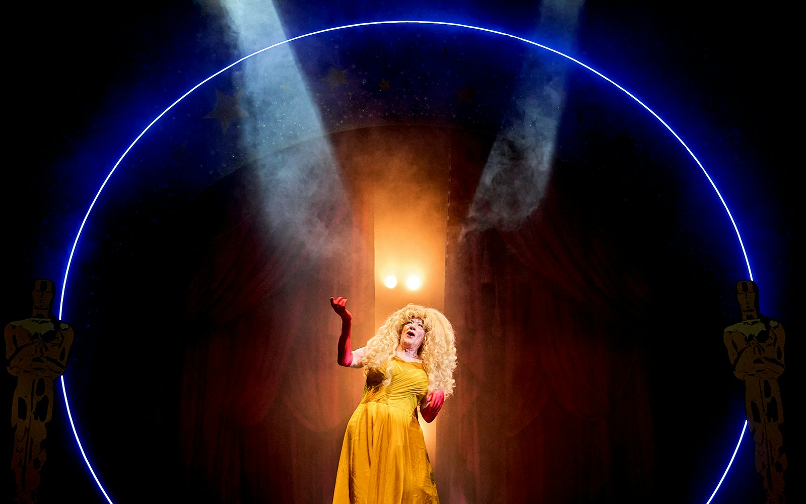 Performer in a yellow dress on stage under spotlight, Mother Goose theme.