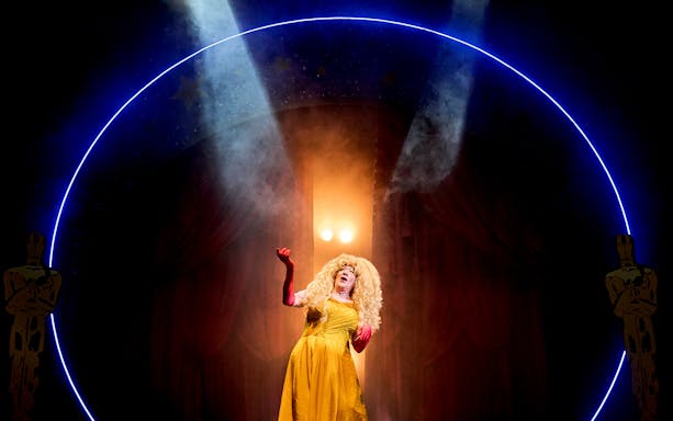 Performer in a yellow dress on stage under spotlight, Mother Goose theme.