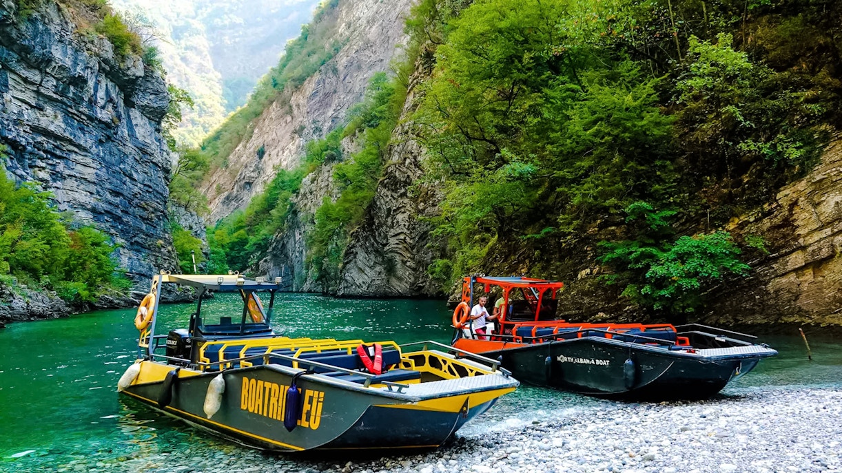 Boats on Komani Lake surrounded by lush cliffs during Shala River tour.