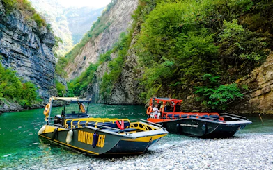 Boats on Komani Lake surrounded by lush cliffs during Shala River tour.