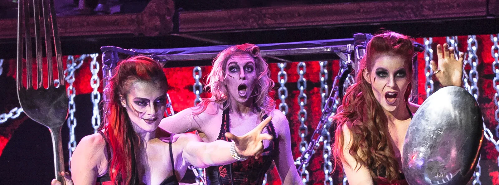 Performers in zombie-themed burlesque show with oversized fork and spoon props.