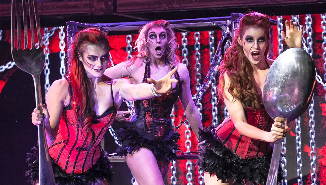 Performers in zombie-themed burlesque show with oversized fork and spoon props.