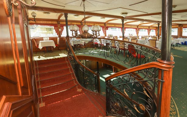 Interior of a Budapest Danube sightseeing cruise ship with dining tables and ornate staircase.