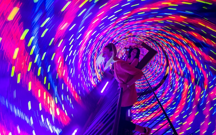 Visitors experiencing a colorful vortex tunnel with swirling lights.
