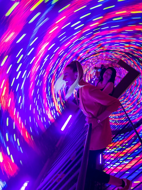 Visitors experiencing a colorful vortex tunnel with swirling lights.