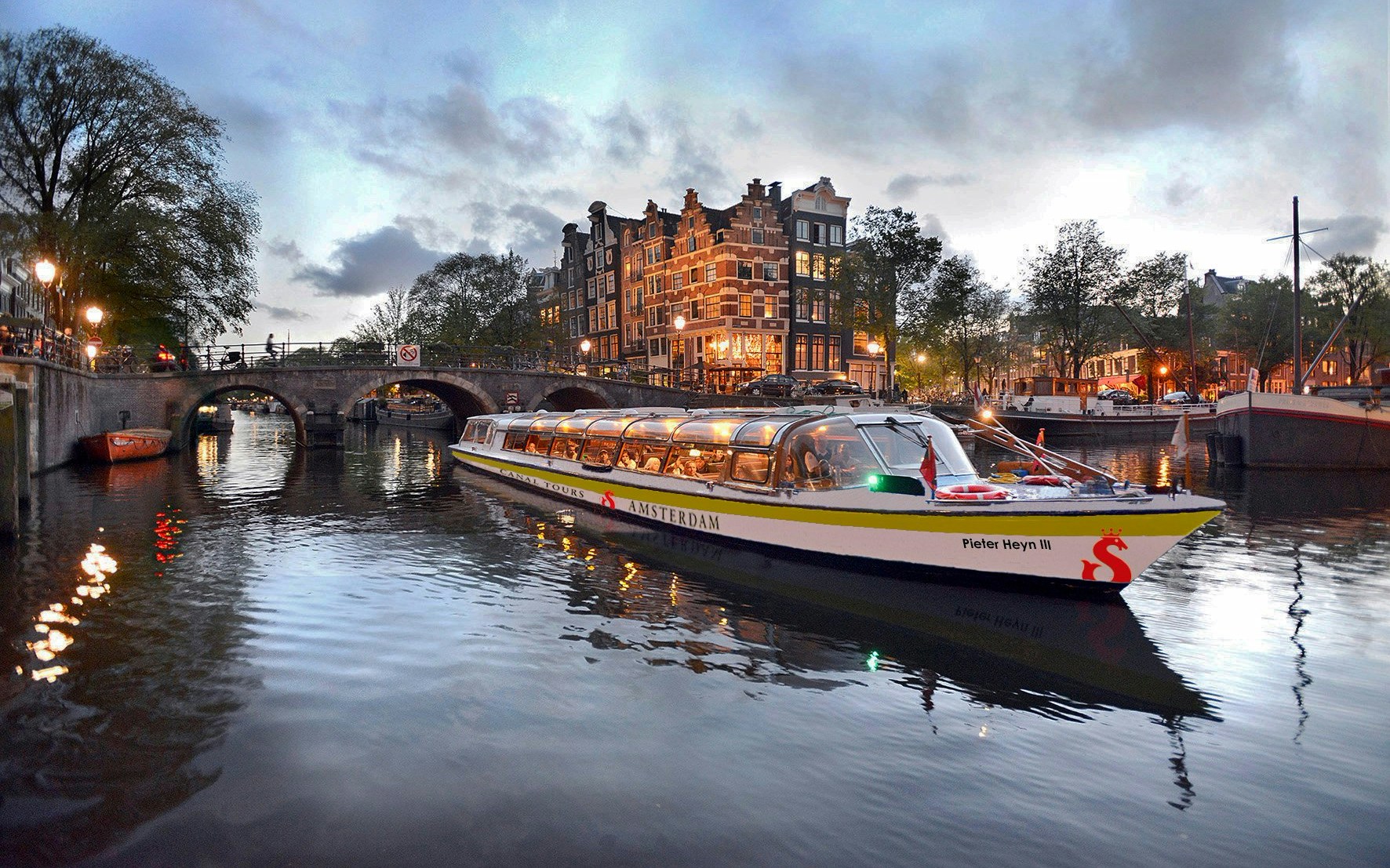 Canal boat cruising through Amsterdam's illuminated canals at dusk.