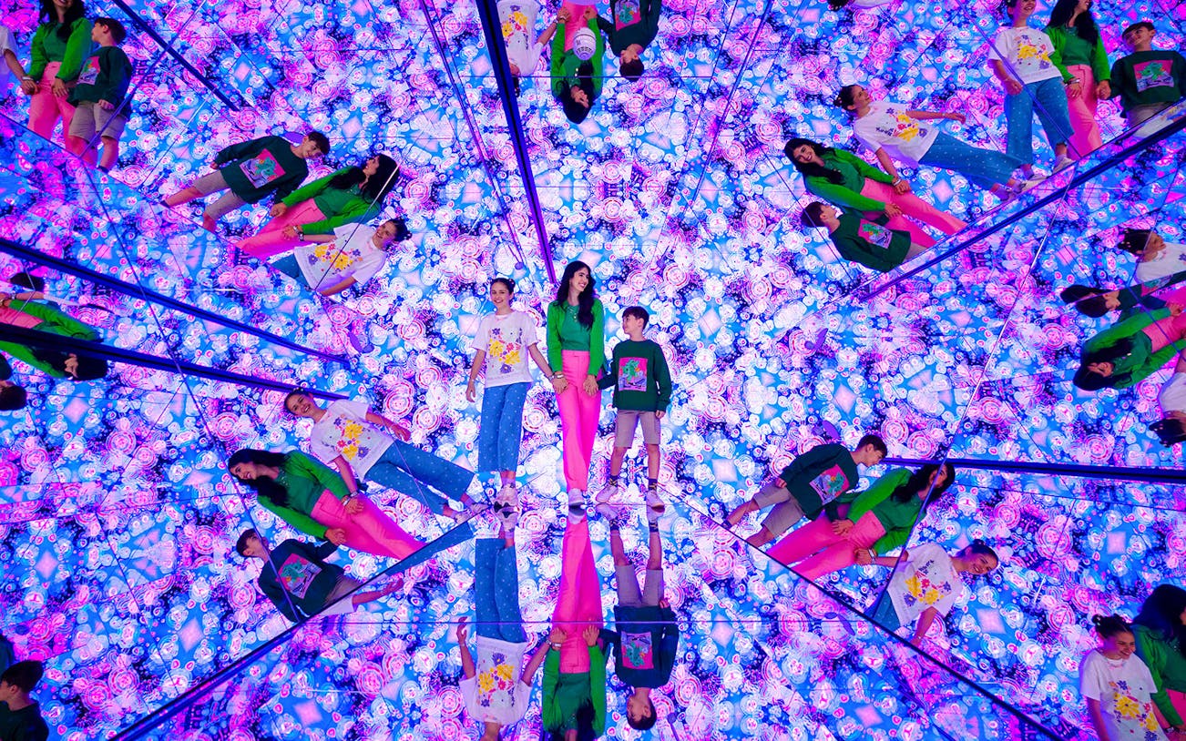 Tourists exploring mirrored room with vibrant lights at House of Hype, Dubai.