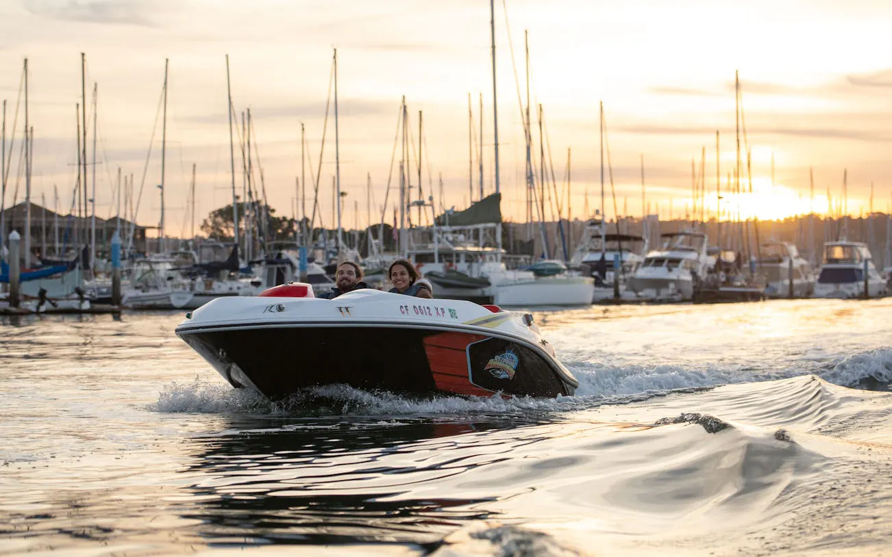 Speed boat on San Diego harbor at sunset with marina in background.