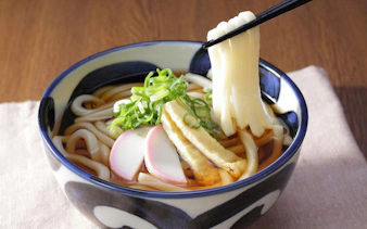 Bowl of Kake Udon with sliced fish cake, green onions, and chopsticks.