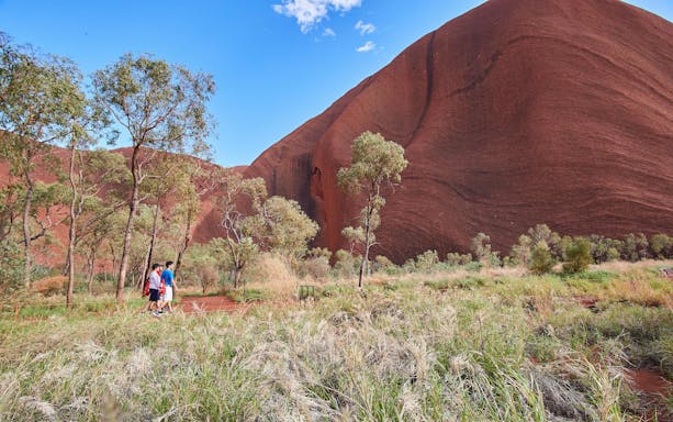 Visitors walking along a trail with Uluru in the background during a sunrise tour.