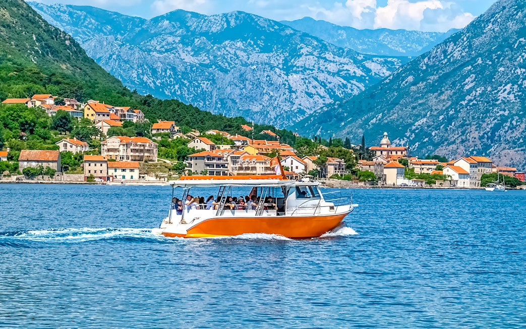 Speedboat on Kotor Bay with coastal village and mountains in Montenegro.