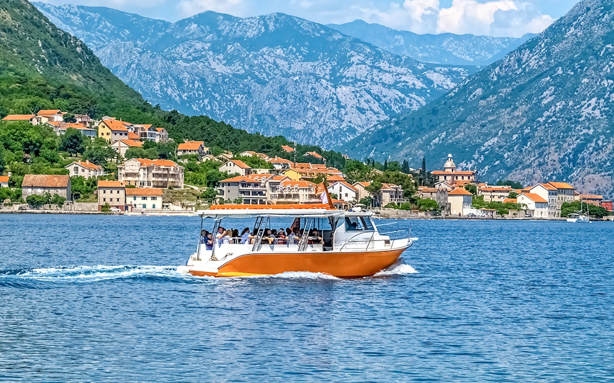 Speedboat on Kotor Bay with coastal village and mountains in Montenegro.