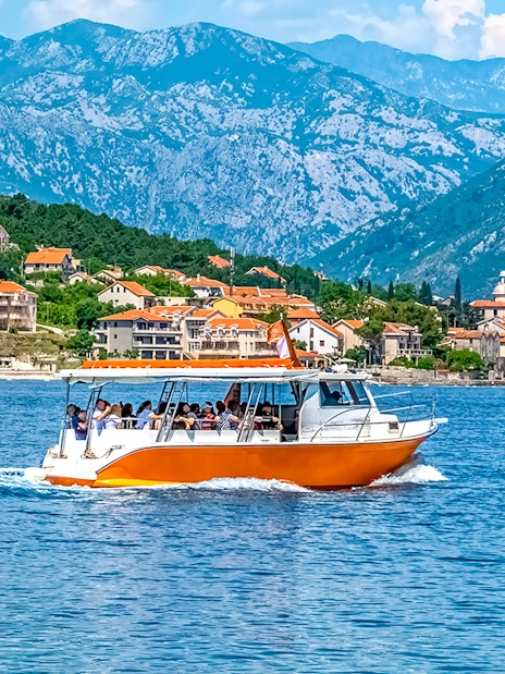 Speedboat on Kotor Bay with coastal village and mountains in Montenegro.