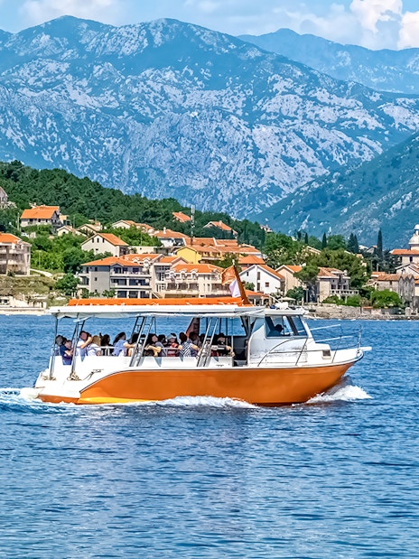 Speedboat on Kotor Bay with coastal village and mountains in Montenegro.