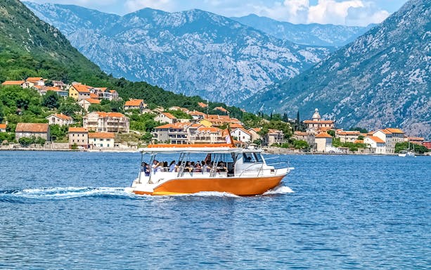 Speedboat on Kotor Bay with coastal village and mountains in Montenegro.